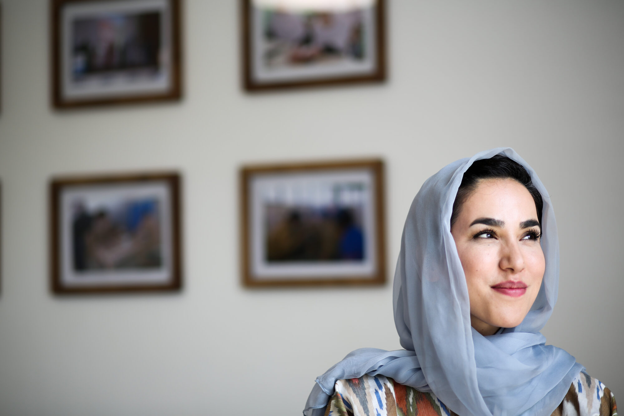 Photo of an Afghani woman with a wall of photos behind her