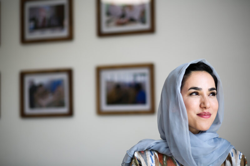 Photo of an Afghani woman with a wall of photos behind her